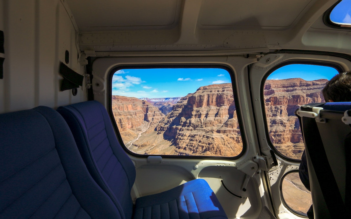 View of the Grand Canyon through a plane window, showcasing rugged cliffs and blue sky.