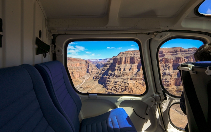View of the Grand Canyon through a plane window, showcasing rugged cliffs and blue sky.