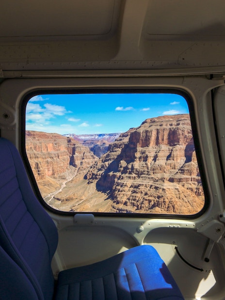 View of the Grand Canyon through a plane window, showcasing rugged cliffs and blue sky.