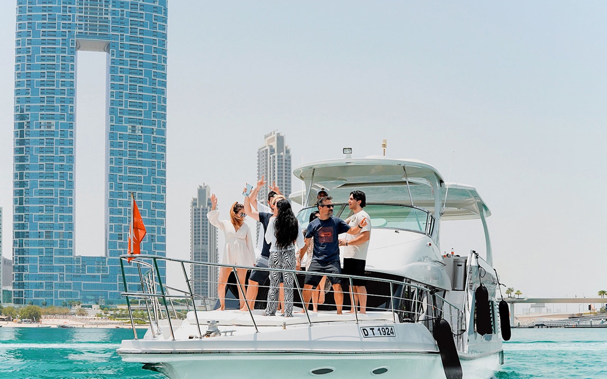 Yacht with people enjoying near JBR, Dubai skyline in background.