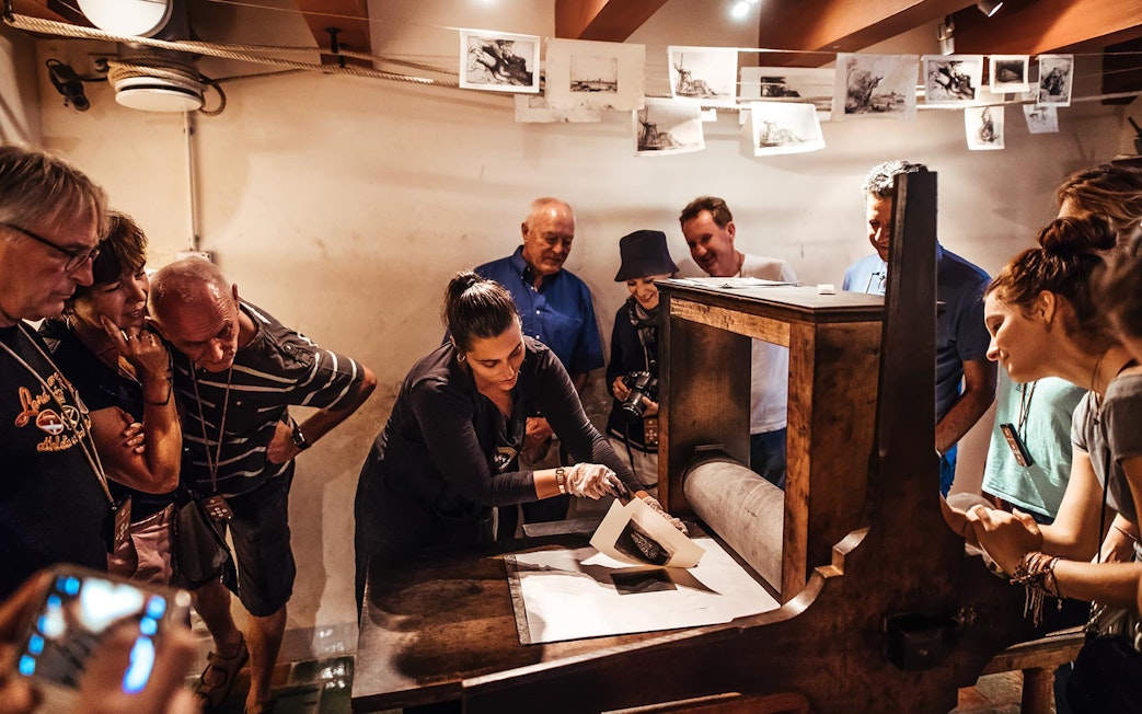 Guide demonstrating printmaking to visitors at Rembrandt House Museum.