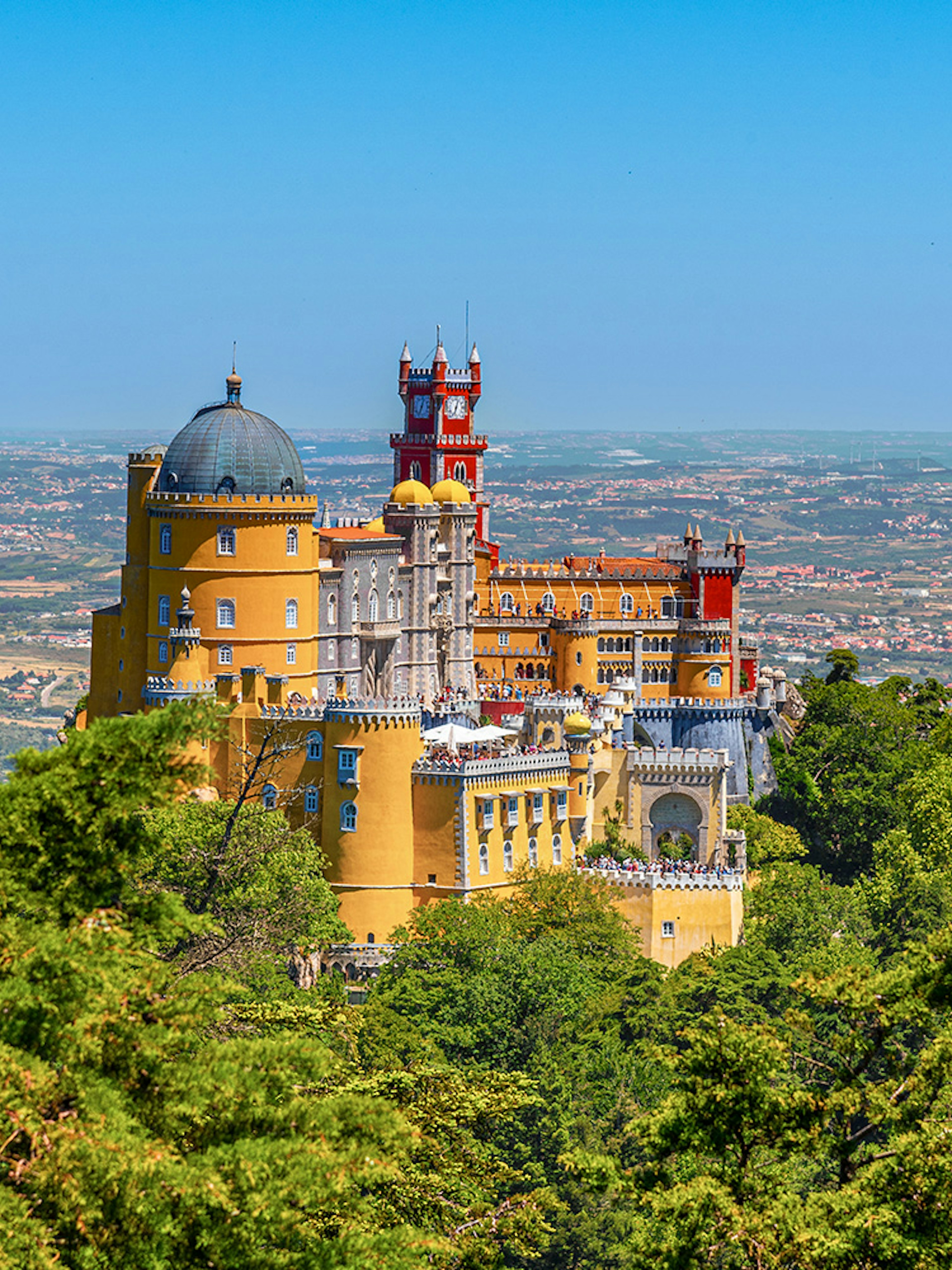 Pena Palace in Lisbon surrounded by lush greenery and overlooking the cityscape.