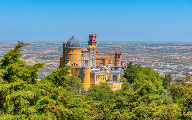 Pena Palace in Lisbon surrounded by lush greenery and overlooking the cityscape.