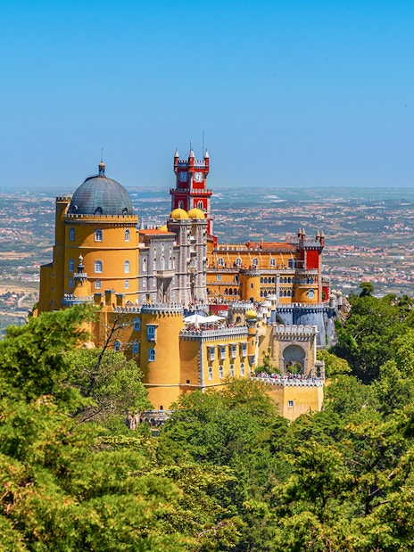 Pena Palace in Lisbon surrounded by lush greenery and overlooking the cityscape.