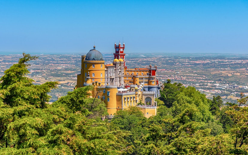 Pena Palace in Lisbon surrounded by lush greenery and overlooking the cityscape.