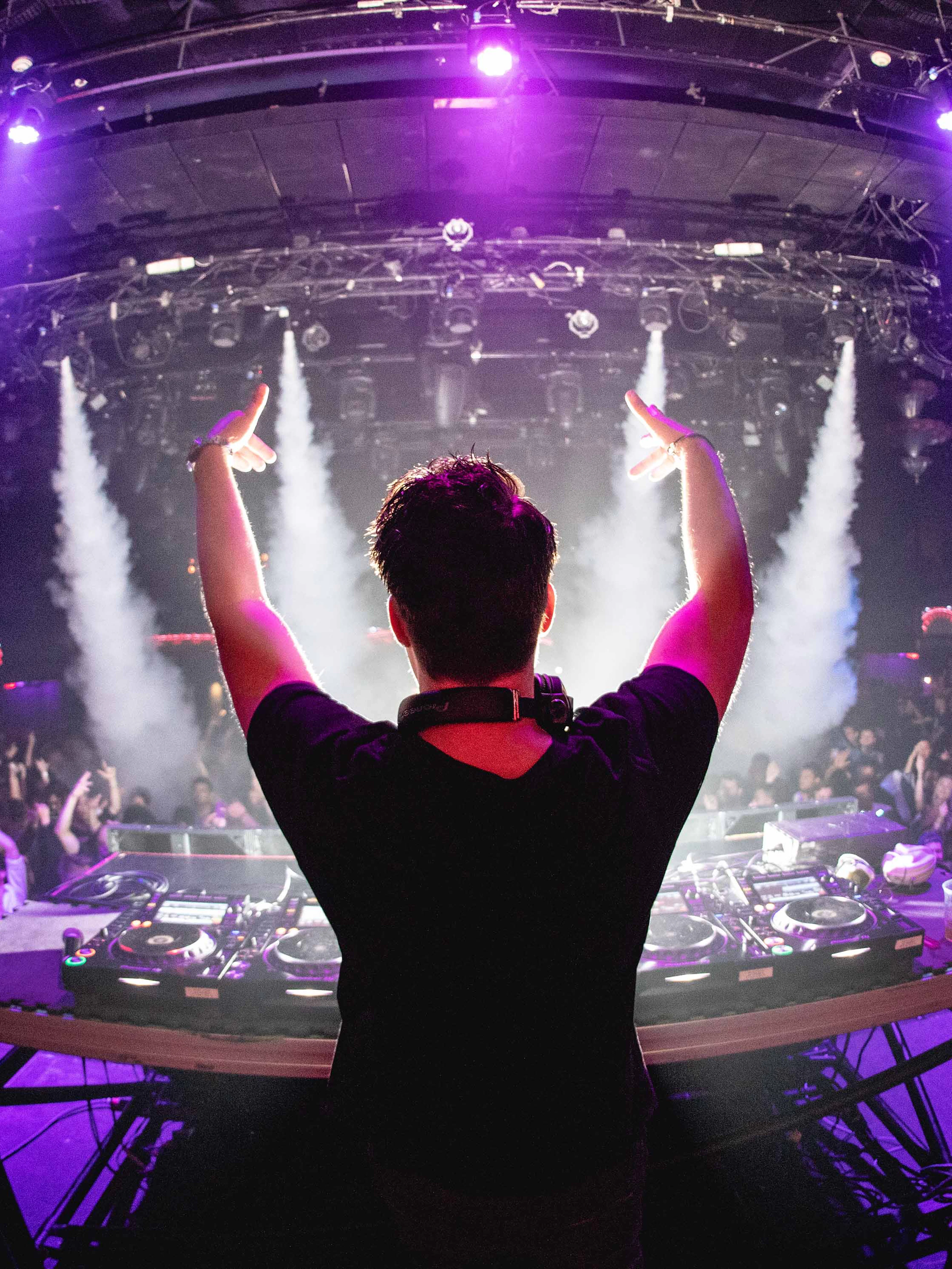 DJ performing at a vibrant party with a cheering crowd and colorful lights.