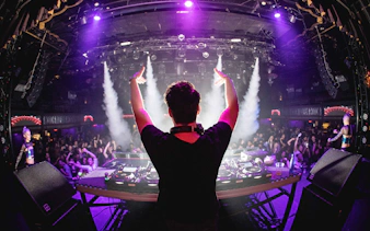 DJ performing at a vibrant party with a cheering crowd and colorful lights.