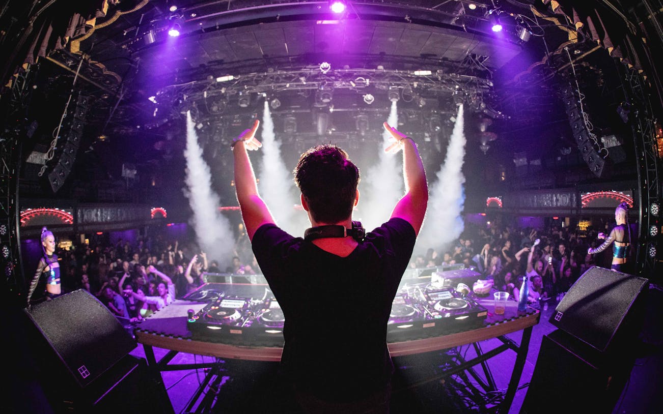 DJ performing at a vibrant party with a cheering crowd and colorful lights.