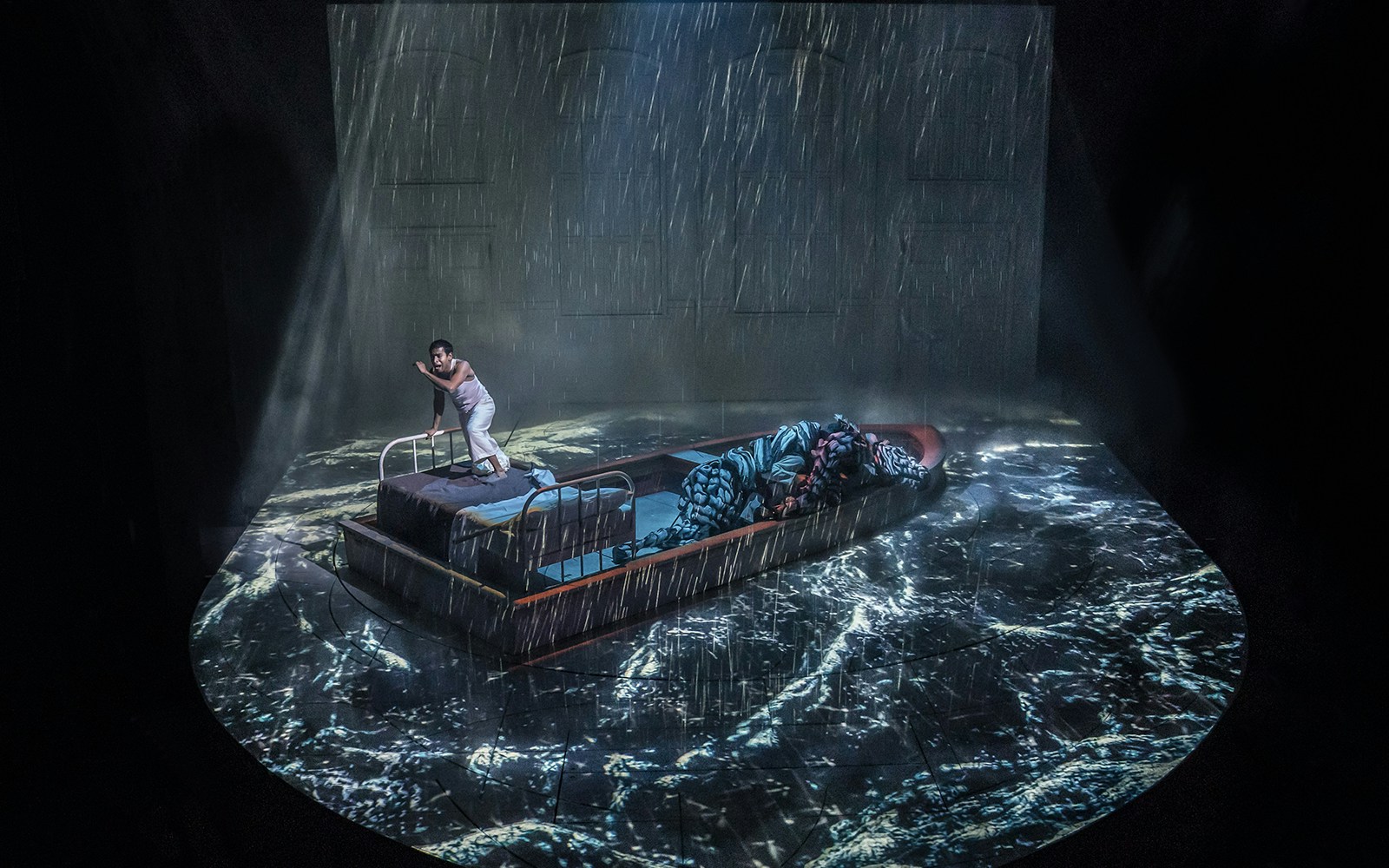 Stage scene from "Life of Pi" with a person on a boat in a stormy sea projection.