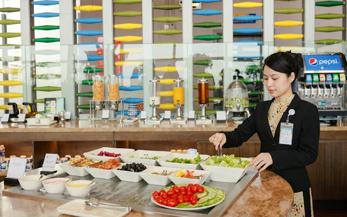 Buffet selection at SH Premium Lounge, Noi Bai International Airport, Hanoi, with staff serving salad.
