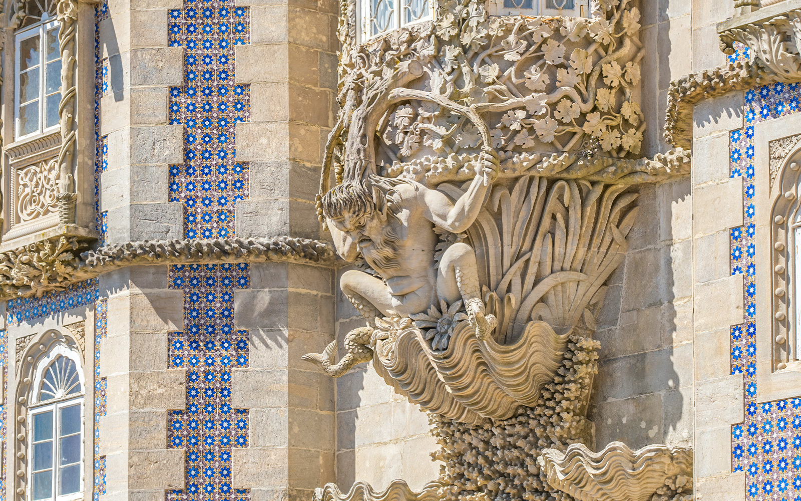 Facade detail of Pena Palace in Sintra, Portugal, featuring intricate stone carvings and blue tilework.
