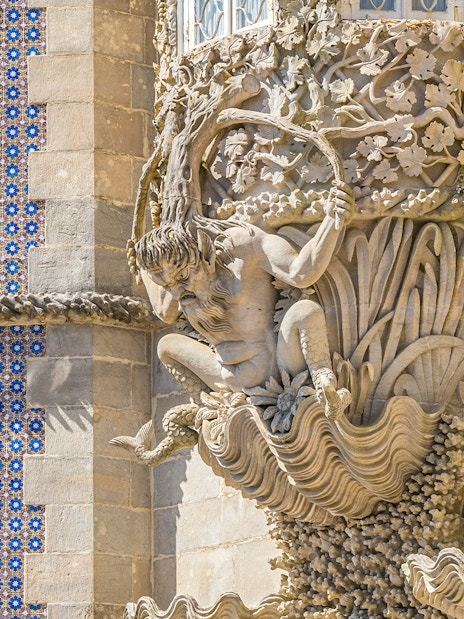 Facade detail of Pena Palace in Sintra, Portugal, featuring intricate stone carvings and blue tilework.