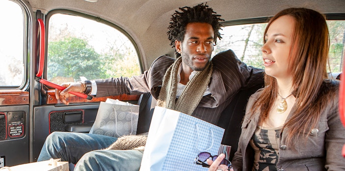 Couple sitting inside a London black cab with shopping bags.
