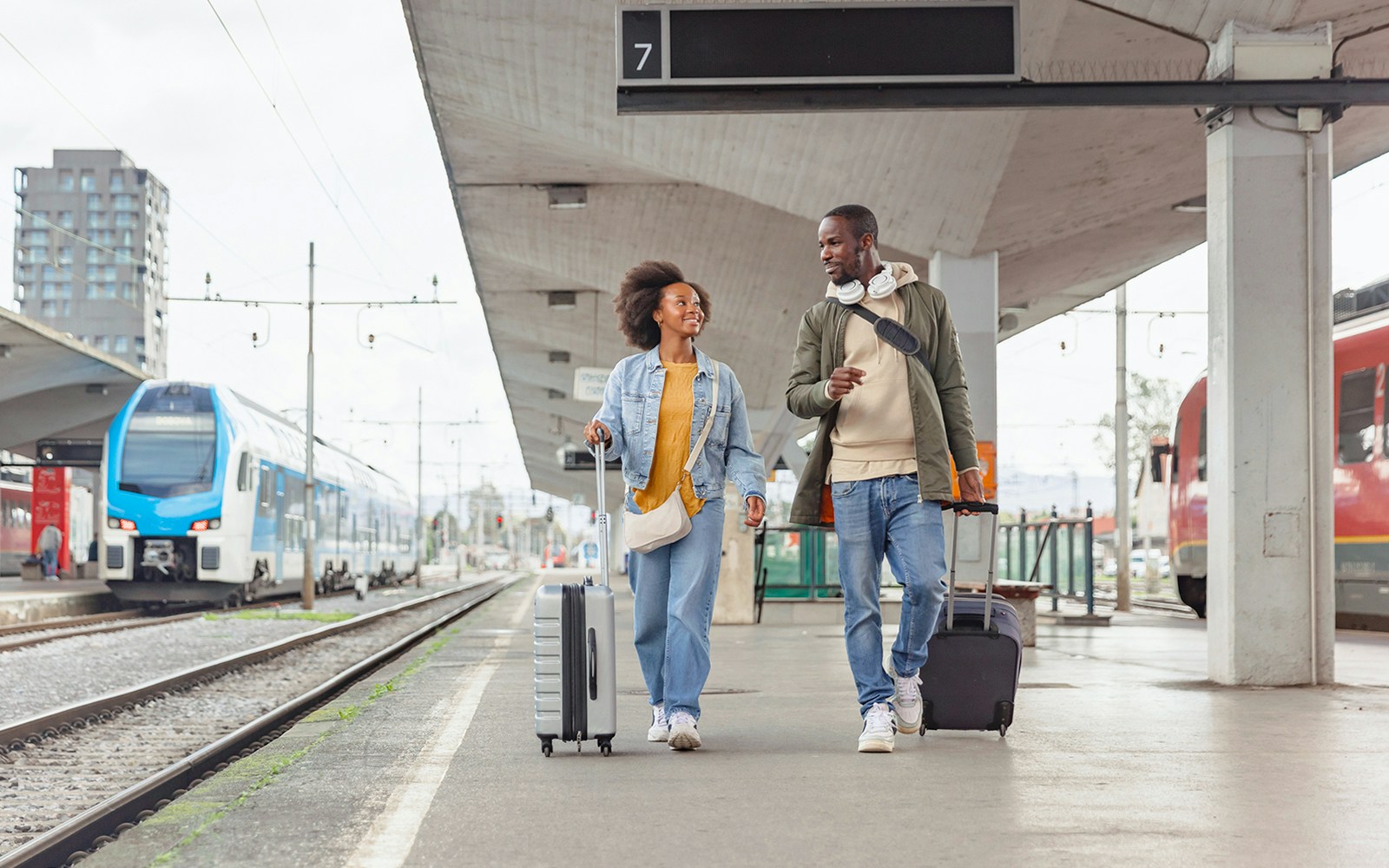 Couple with suitcases walking through a bustling train station in Europe.