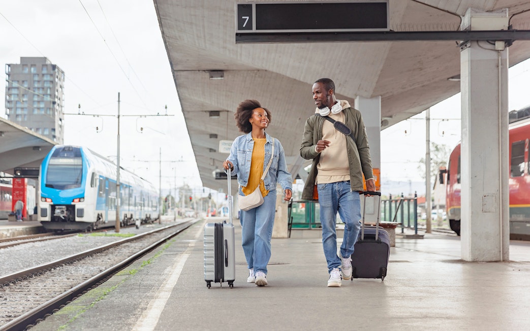 Couple walking with luggage at a train station platform.
