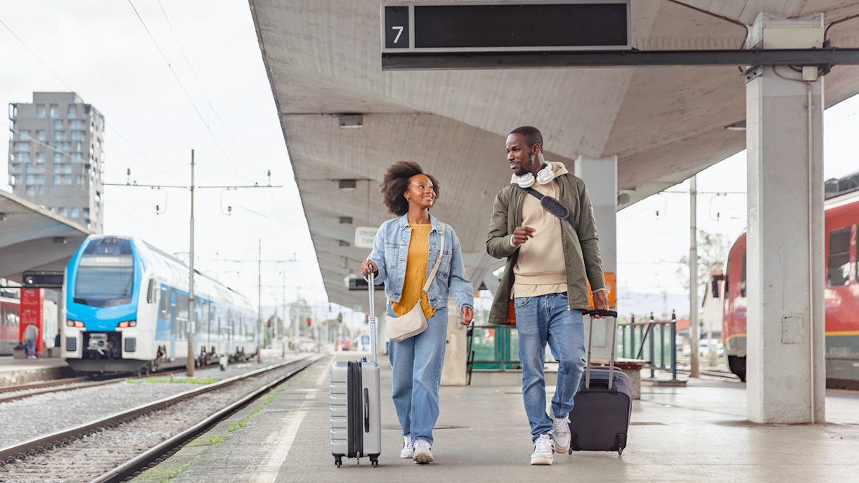 Couple walking with luggage at a train station platform.