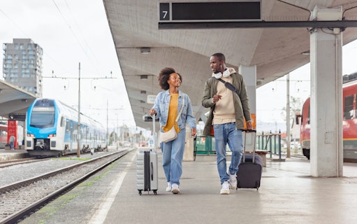 Couple walking with luggage at a train station platform.