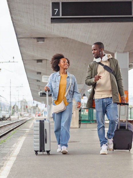Couple walking with luggage at a train station platform.