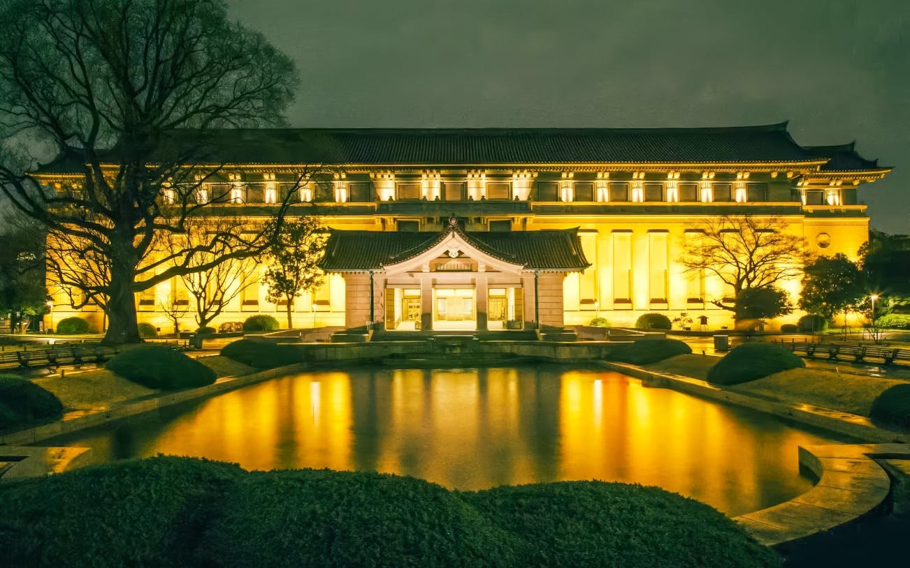 Honkan of Tokyo National Museum illuminated at night with reflection in pond.