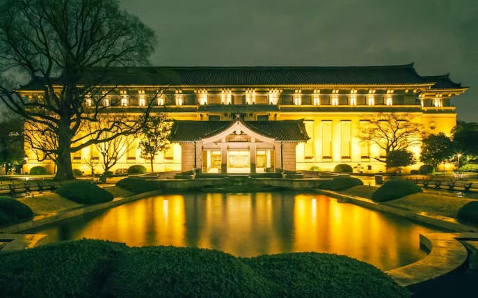 Honkan of Tokyo National Museum illuminated at night with reflection in pond.