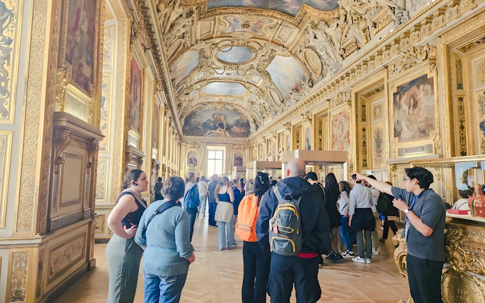 Visitors exploring ornate gallery inside Louvre Museum, Paris, France.
