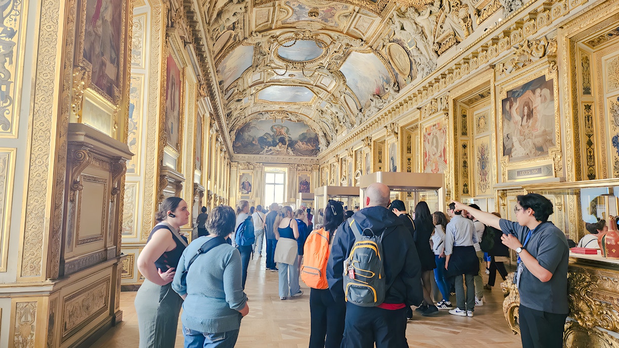 Visitors exploring ornate gallery inside Louvre Museum, Paris, France.