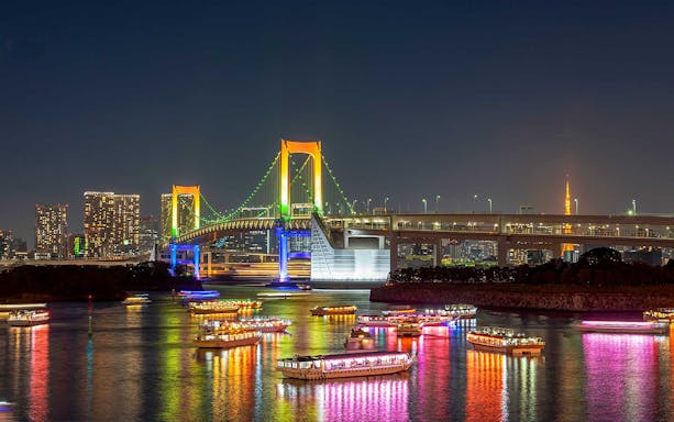 Tokyo night cruise with illuminated boats on the water near Rainbow Bridge.