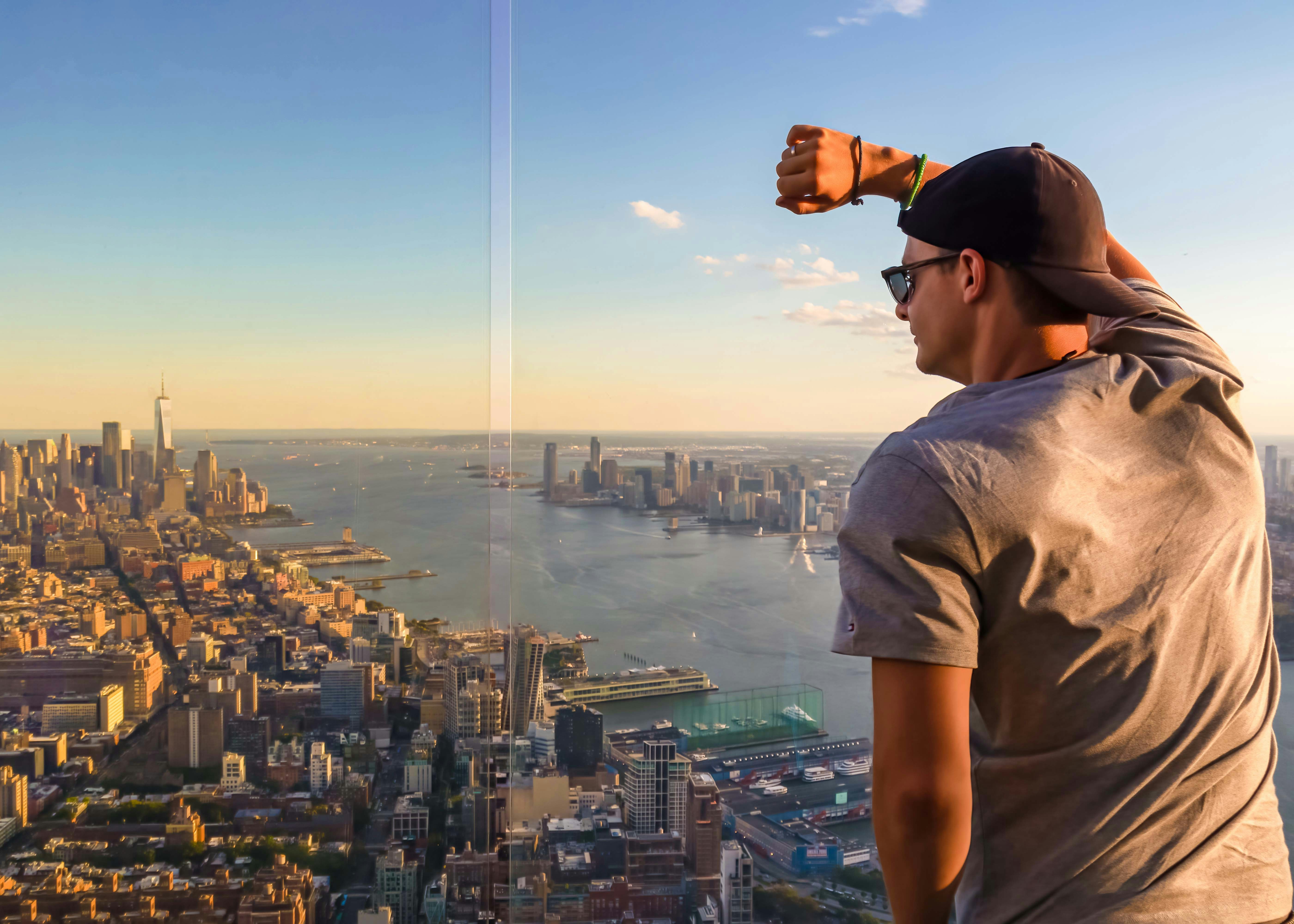 Person enjoying the view from One World Observatory, overlooking New York City skyline and Hudson River.
