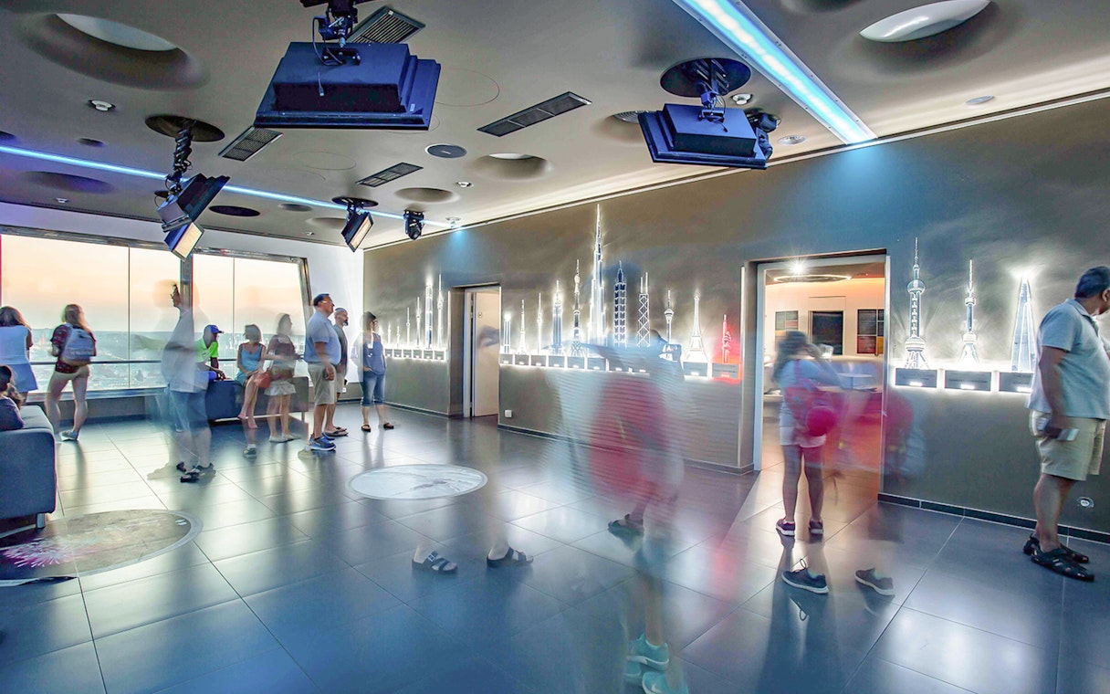 Visitors inside Žižkov Television Tower observation deck, Prague, with skyline models.