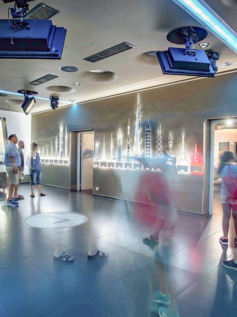 Visitors inside Žižkov Television Tower observation deck, Prague, with skyline models.