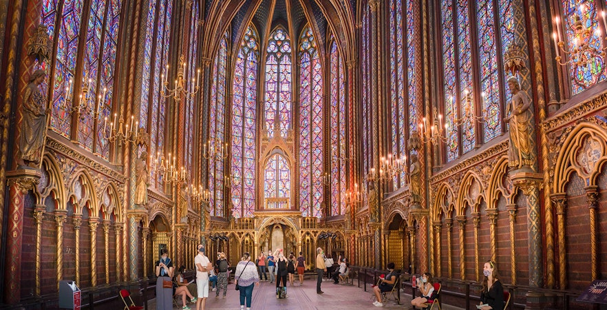 Visitors inside Sainte-Chapelle, Paris, admiring stained glass windows and Gothic architecture.