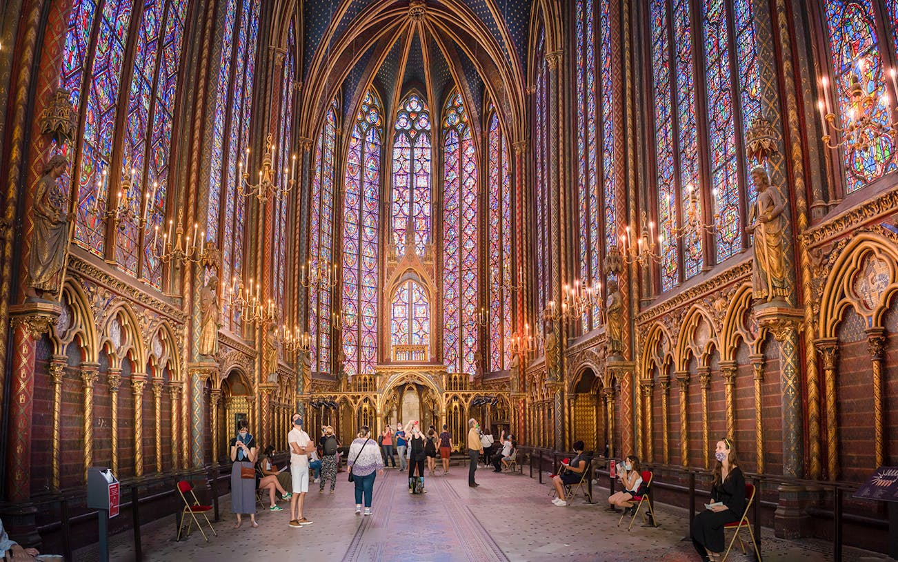 Visitors inside Sainte-Chapelle, Paris, admiring stained glass windows and Gothic architecture.