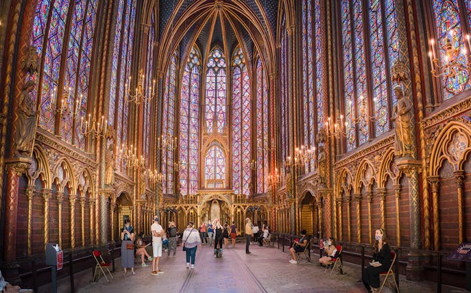 Visitors inside Sainte-Chapelle, Paris, admiring stained glass windows and Gothic architecture.