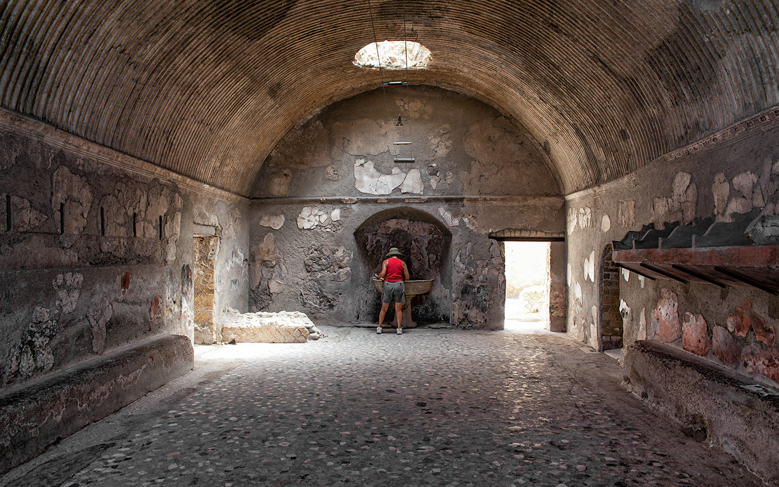 Tourist exploring ancient Herculaneum baths interior, Italy.
