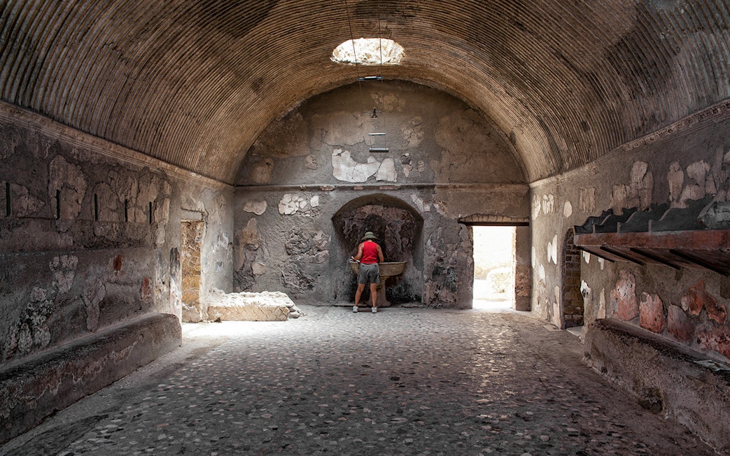 Tourist exploring ancient Herculaneum baths interior, Italy.