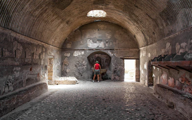 Tourist exploring ancient Herculaneum baths interior, Italy.