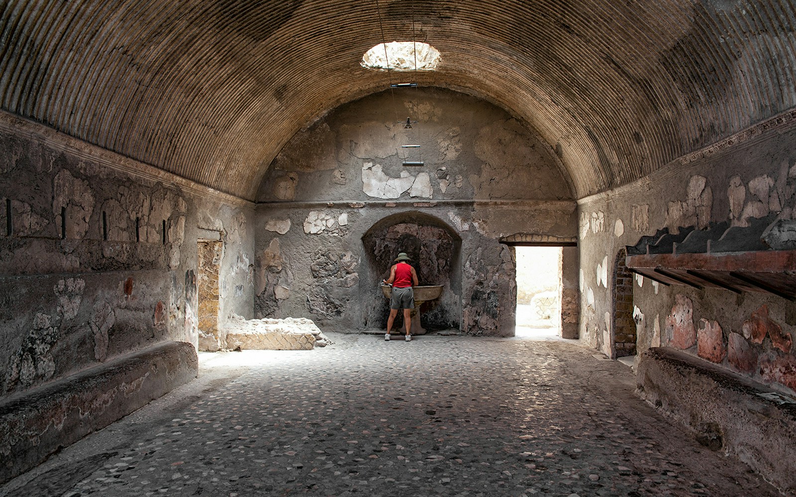 Tourist exploring ancient Herculaneum baths interior, Italy.