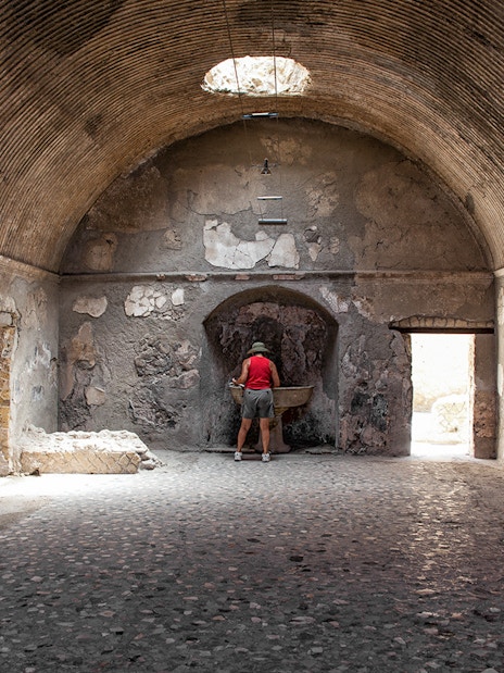 Tourist exploring ancient Herculaneum baths interior, Italy.