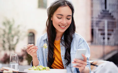Woman using smartphone while eating salad at outdoor cafe.