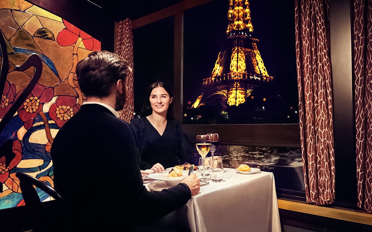 Couple dining on Maxim's Seine River Cruise with Eiffel Tower view.