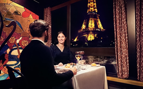 Couple dining on Maxim's Seine River Cruise with Eiffel Tower view.