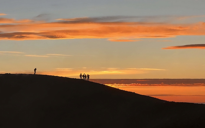 Hikers silhouetted against a sunset at Mount Etna.