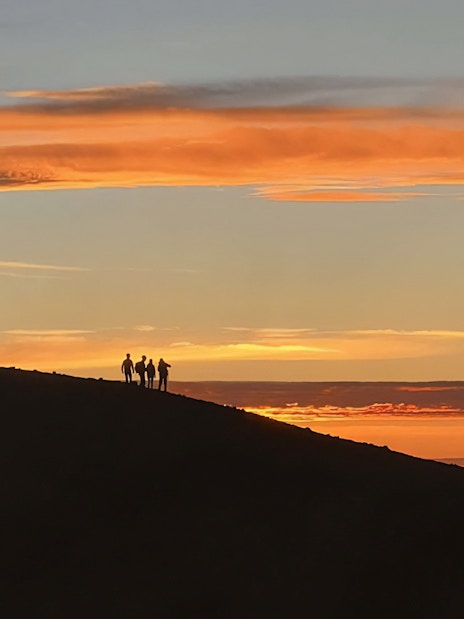 Hikers silhouetted against a sunset at Mount Etna.