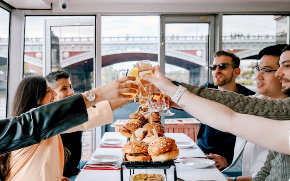 Guests toasting with drinks on a brunch cruise in Melbourne, with burgers on the table.