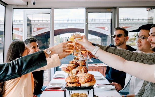 Guests toasting with drinks on a brunch cruise in Melbourne, with burgers on the table.