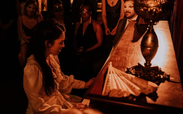 Pianist performing at Masquerade Broadway with masked audience.