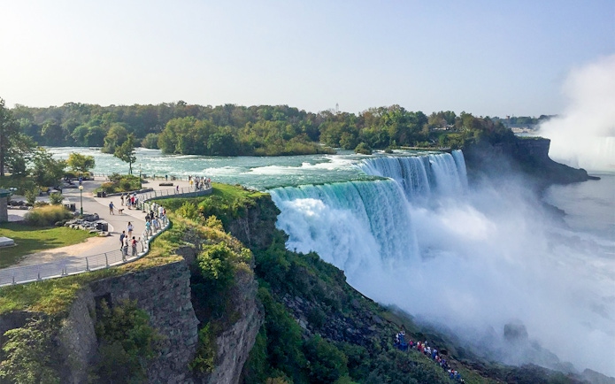 Aerial view of Niagara Falls with tourists on a walkway and lush greenery.