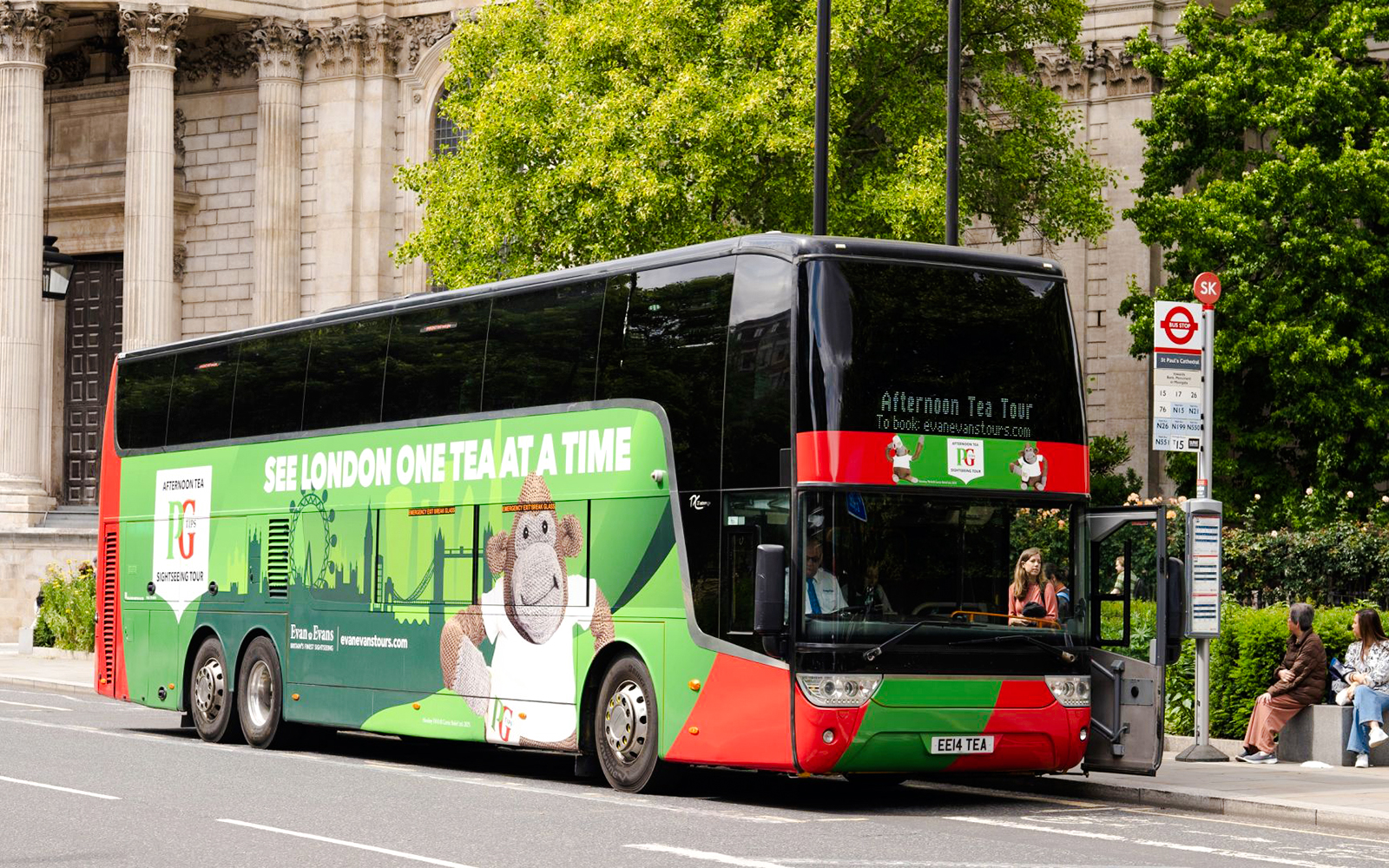 Double-decker bus for Afternoon Tea Sightseeing Tour in London, parked near historic building.