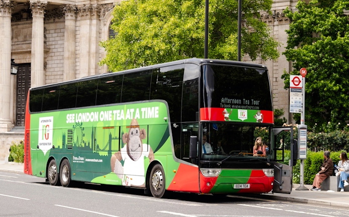 Double-decker bus for Afternoon Tea Sightseeing Tour in London, parked near historic building.