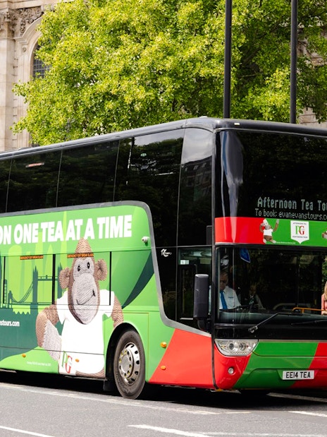 Double-decker bus for Afternoon Tea Sightseeing Tour in London, parked near historic building.